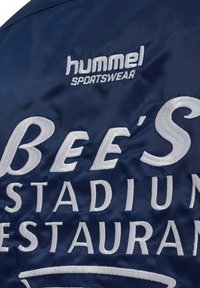 Navy blue satin jacket featuring white embroidered text: "hummel SPORTSWEAR" and "BEE'S STADIUM RESTAURANT." Smooth texture, sporty design.