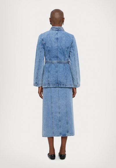 Lyseblå denimjakke med peplumliv og lange ermer, parret med et matchende denimmaxikjørt. Silkeaktig tekstur, synlige sømdetaljer.