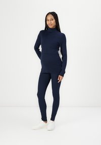 Maglione a collo alto in maglia navy abbinato a leggings coordinati, caratterizzato da una texture liscia e una silhouette aderente, completato da sneakers bianche.
