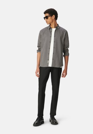 Camisa a rayas en blanco y negro, con cuello y botones, combinada con pantalones negros ajustados y zapatos negros, acompañada de gafas de sol oscuras.