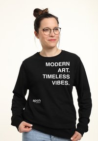 Felpa nera con testo bianco "ARTE MODERNA. VIBRAZIONI ETERNE." e logo "apoh London" in basso a sinistra. Presenta un classico design con colletto a girocollo.
