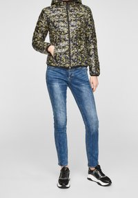 Polstret sort jakke med blomstermotiv, lynlåslukning og hætte. Bæres med blå stramme jeans og sorte sneakers med hvide såler.