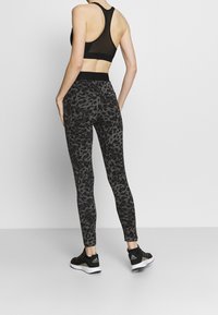 Reggiseno sportivo in rete nera e leggings neri con stampa leopardata, caratterizzati da un design a vita alta e aderente, abbinati a scarpe da ginnastica nere.