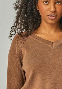 Brauner gerippter Pullover mit V-Ausschnitt, der Texturvariationen und eingesetzten Ärmeln aufweist. Hergestellt aus weichem Strickmaterial.