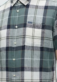 Chemise à manches courtes boutonnée avec motif à carreaux vert, bleu marine, blanc et gris et poche poitrine avec petite étiquette logo Barbour.