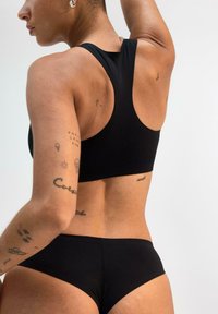 Set di reggiseno sportivo nero e slip bikini, realizzato in materiale liscio e elasticizzato. Presenta un design a schiena scoperta e una linea bassa con uno stile minimalista.