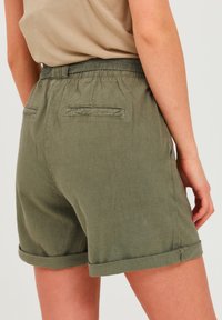 Olive green, elastic waistband shorts with rolled hems and two back pockets. Made of lightweight fabric with a textured finish.