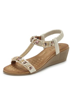Beige wedge sandal with cushioned footbed, gold chain and pearl decorations on straps, and elastic back strap for secure fit.