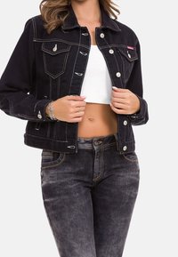 Schwarze Denimjacke mit kontrastierenden weißen Nähten, Fronttaschen und Metallknöpfen, kombiniert mit dunkelblauen Jeans und einem weißen Crop-Top.