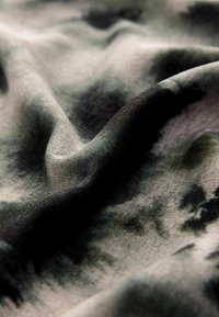 Struktureret stof i nuancer af grå og sort med et subtilt tie-dye mønster. Materialet virker let og falder blødt.
