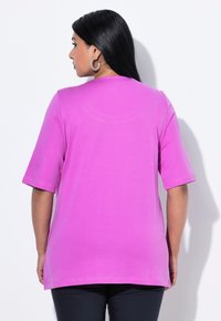 Fuchsia kortærmet skjorte lavet af blødt stof, med rund halsudskæring og lige snit, båret med mørke bukser.