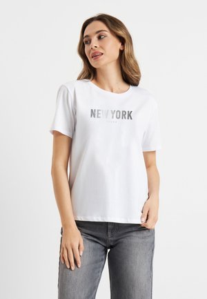 Witte katoenen T-shirt met een zilveren "NEW YORK" grafische print. Ronde halslijn, korte mouwen, relaxte pasvorm. Ggedragen met grijze jeans.