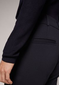 Pantalon bleu marine foncé en tissu lisse, coupe slim, avec une poche arrière et des coutures détaillées le long des coutures.