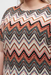 Prim-plan cu o bluză de damă cu model zigzag multicolor în nuanțe de ruginiu, negru, roz, albastru și bej.