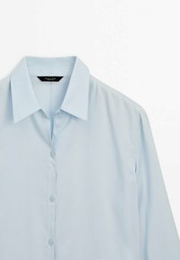 Chemise bleu clair à manches longues avec col pointu, boutonnée, présentée à plat sur fond blanc.