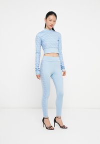 Világoskék sportos szett, mintás, hosszú ujjú crop top-pal és hozzáillő leggings-szel, sima textúrával és testhezálló fazonnal. Fekete, pántos magassarkú cipők.