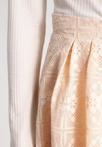 Vaaleanpunaista pitsihame, jossa on monimutkaisia kukkakuosia, laskoksia ja teksturoitu vyötärö, yhdistettynä vaaleanharmaaseen ribbikankaiseen pitkähihaiseen p topiin.