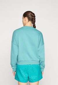 Turkos sweatshirt med sänkta axlar, rund halsringning och ribbad fåll, matchad med mönstrade akvablå shorts. Slät textur, avslappnad passform.