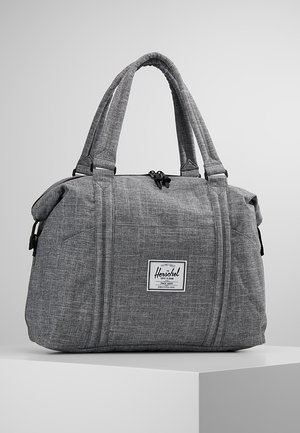 Sac de voyage Herschel en tissu gris avec doubles poignées, fermeture éclair et étiquette de marque à l'avant, posé sur une plateforme blanche sur un fond uni.