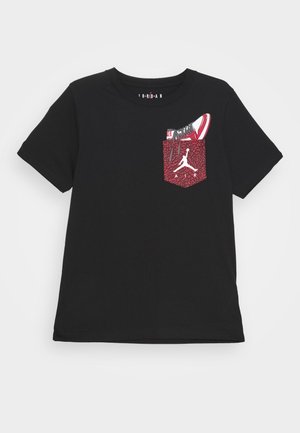 T-shirt nera a maniche corte con tasca rossa testurizzata con logo Jumpman bianco e grafica di una sneaker rossa e bianca che sporge dalla tasca.