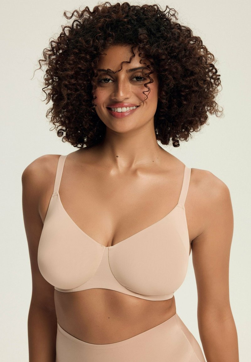 Beżowy bezprzewodowy stanik z gładkiego materiału, cienkimi regulowanymi ramiączkami i uformowanymi miseczkami. Prosty design bez wzorów, zapewniający gładki wygląd.
