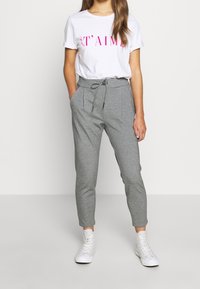 Lichtgrijze tapered sweatpants met een verstelbare tailleband, zijzakken en plooien; gecombineerd met een wit T-shirt met roze tekst.