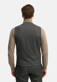 Grå tekstureret vest med slankt design, båret over en beige langærmet skjorte. Vist fra bagsiden, med en glat overflade og minimale detaljer.