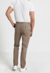 Beżowe chinosy slim-fit z tylnymi kieszeniami, wykonane z mieszanki bawełnianej. Połączone z białą koszulką i białymi trampkami.