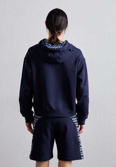 Sweatshirt azul marinho com interior texturizado e calções combinando com detalhes em zigzag em verde e azul. O design é casual e funcional.