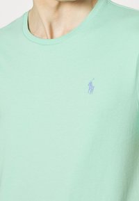 Mintgroene katoenen t-shirt met een ronde hals en korte mouwen. Bevat een klein geborduurd logo in paars op de linkerkant van de borst.