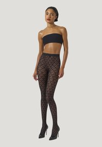 Calze nere a fantasia con un design a ragnatela, indossate con un top bandeau nero e tacchi alti, che mettono in evidenza dettagli intricati e texture.