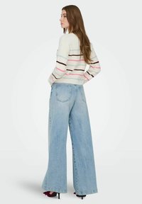 Håndstrikket hvit genser med rosa, brune og blå striper; kombinert med lyseblå vide jeans og svarte høye hæler.