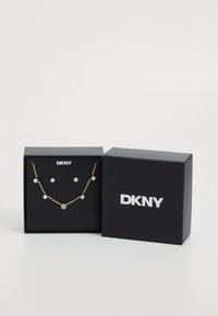 Set di gioielli in tono oro composto da una collana con accenti circolari in cristallo e orecchini a bottone coordinati, presentato in una scatola firmata DKNY.