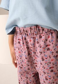 Helles blaues T-Shirt kombiniert mit rosa cordartigen Hosen mit Blumenmuster, die einen elastischen Bund und kleine, bunte Blumenmuster aufweisen.