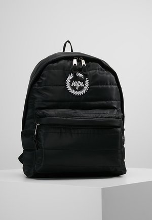 Sac à dos noir matelassé avec poche avant zippée, deux curseurs de zip en haut, et logo circulaire blanc avec le texte "hype." et motif de couronne de laurier.