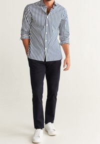 Camicia a colletto con sottili righe navy e bianche, maniche lunghe, abbottonatura, abbinata a pantaloni scuri e sneakers bianchi.