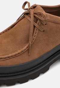 Chaussure en cuir marron à lacets avec une semelle en caoutchouc noir épaisse et des coutures détaillées, vue en gros plan.