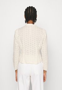 Cremfarbige, kurz geschnittene Jacke mit aufwendigem Lochmuster, langen Ärmeln und taillierter Passform. Strukturiertes Material, klassischer Kragen.