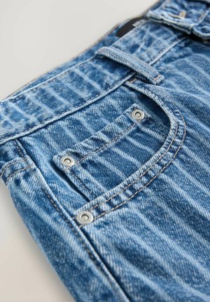 Jeans de mezclilla azul con un acabado texturizado, costuras en contraste y un pequeño bolsillo de parche asegurado con remaches metálicos.