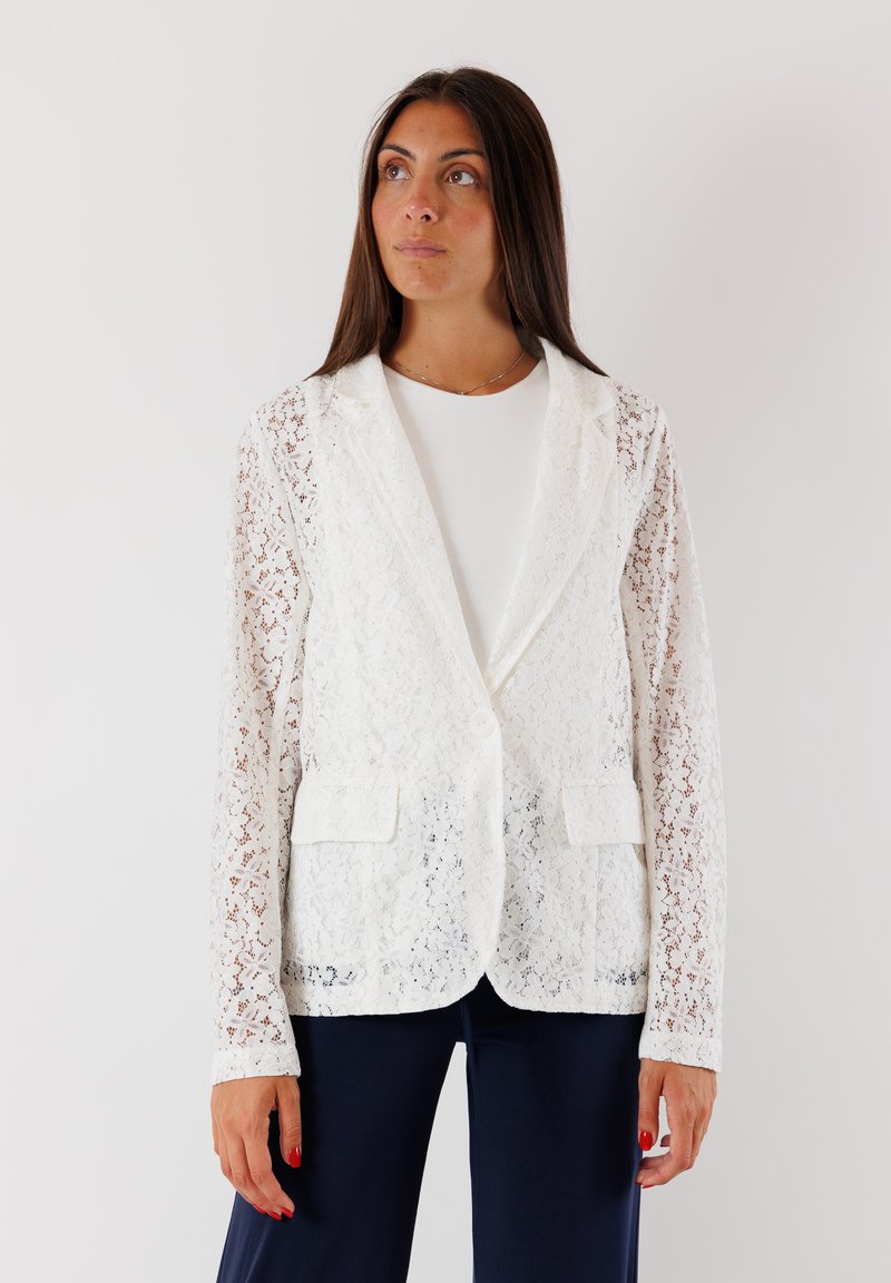Blazer bianco in pizzo con un design sartoriale, dotato di due tasche frontali, chiusura con bottoni e maniche lunghe. Tessuto liscio e materiale leggero.