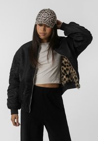 Crna bomber jakna s oblogom od leopard uzorka, prilagođenog dizajna i rebrastim manžetama. Upari sa bež skraćenim topom i crnim hlačama, a na kraju je još tu i kapa s leopard uzorkom.