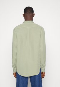 Camicia a maniche lunghe verde chiaro con colletto, dettaglio a piega sul retro, polsini con bottoni e orlo arrotondato, realizzata in un tessuto liscio e strutturato.