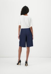 Vit kortärmad topp tillsammans med marinblå högmidjade shorts. Shorts har en enkel design, sidofickor och en mjuk textur. Svarta högklackade skor fulländar looken.