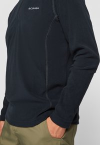 Sort fleece pullover med en kvart lynlås, med et Columbia-logo på brystet og kontrastsyninger langs sømmene.