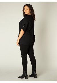 Zwarte, loszittende blouse met opgerolde mouwen, gecombineerd met zwarte skinny jeans en enkellaarsjes. Zacht materiaal, ontspannende silhouet en minimalistisch ontwerp.