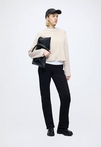Light beige cropped sweater, black pants, black shoes, and a black bag. The subject wears a black cap and has short hair. Simple design.