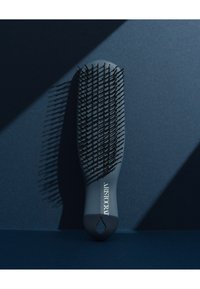 Grå hårbørste med sorte børster, oval form, ergonomisk håndtak, og et opphengshull; har teksten "ARISTOCRAT" i hvitt på håndtaket.