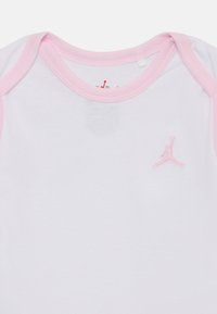 Fehér pamut babarugdalózó rövid rózsaszín ujjakkal, a mellkasán egy kis rózsaszín hímzett Jumpman logóval. Sima textúra.