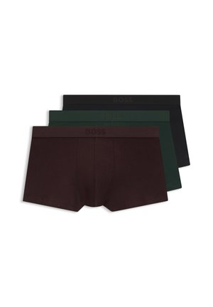 Veltrænet mand med mørk hud iført ensfarvede mørkebrune boksershorts står foran en ensfarvet lys baggrund.