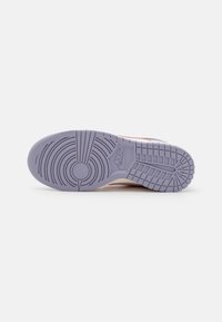 Semelle violette d'une basket Nike montrant des motifs de bandes circulaires et rectangulaires avec le logo Nike au milieu du pied, sur un fond blanc.